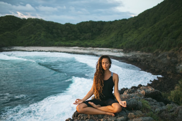 Person sitting cross-legged meditating with eyes closed, practicing mindfulness